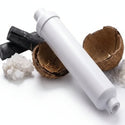 A white ecosoft mineralizing postfilter cartridge with water droplets, displayed diagonally on a white surface with coconut halves, charcoal, and salt crystals. 