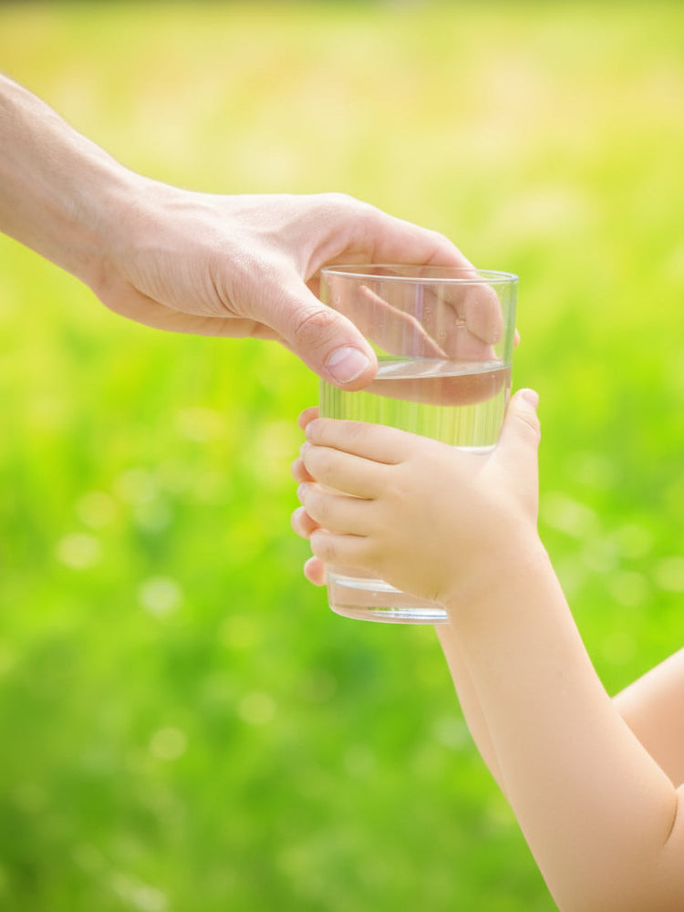 Hand giving a glass of water to another hand against a green outdoor background